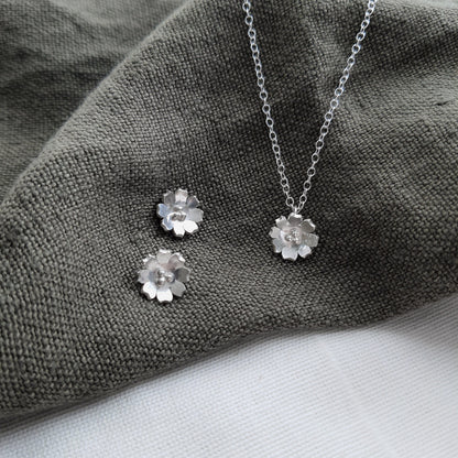 silver flower earrings and necklace on a green fabric background