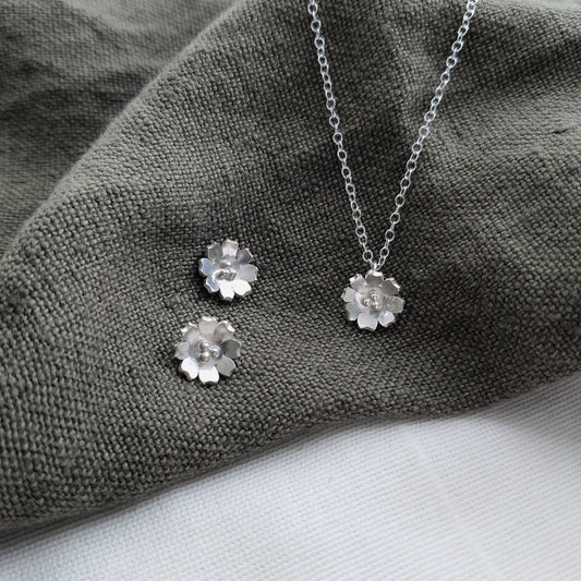 silver flower earrings and necklace on a green fabric background