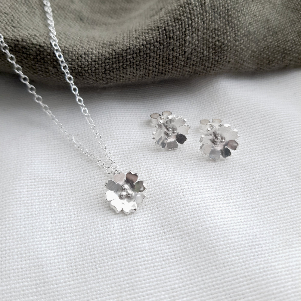 silver flower necklace and matching stud earrings on a white background with som green fabric