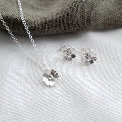 silver flower necklace and matching stud earrings on a white background with som green fabric
