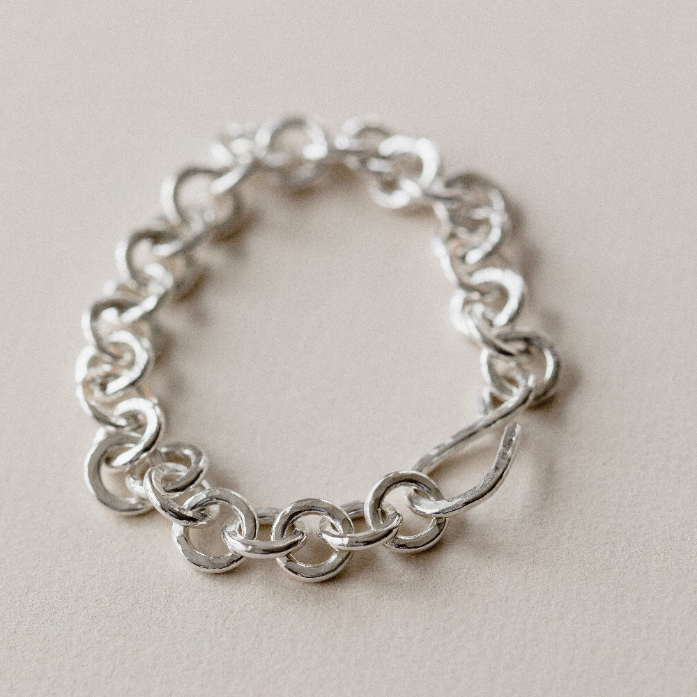 A chunky hammered link silver bracelet on a cream surface