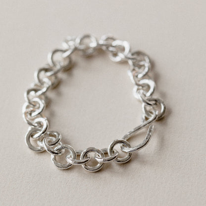 A chunky hammered link silver bracelet on a cream surface