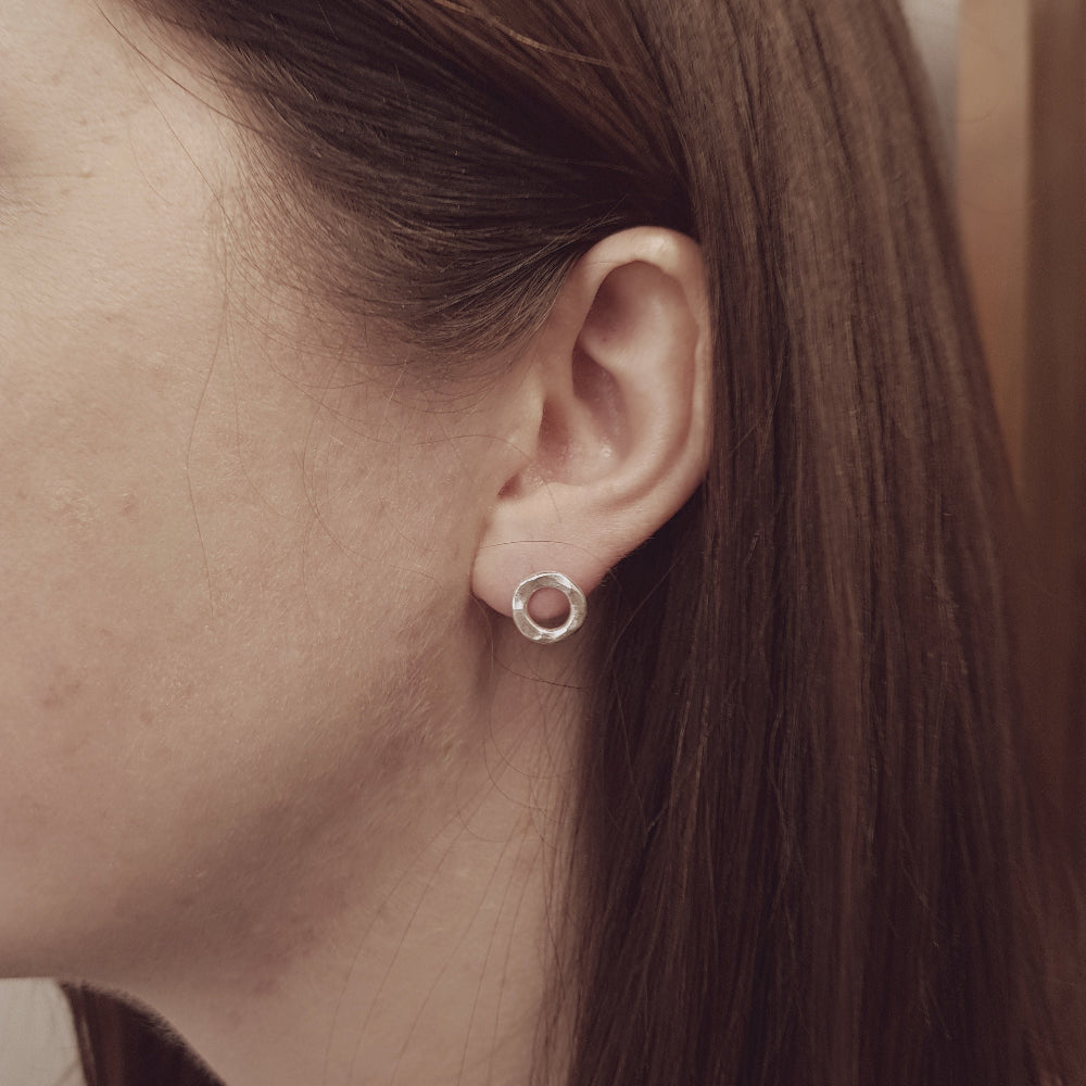 sterling silver hammered circle stud earring being worn in the ear of a lady with long dark hair