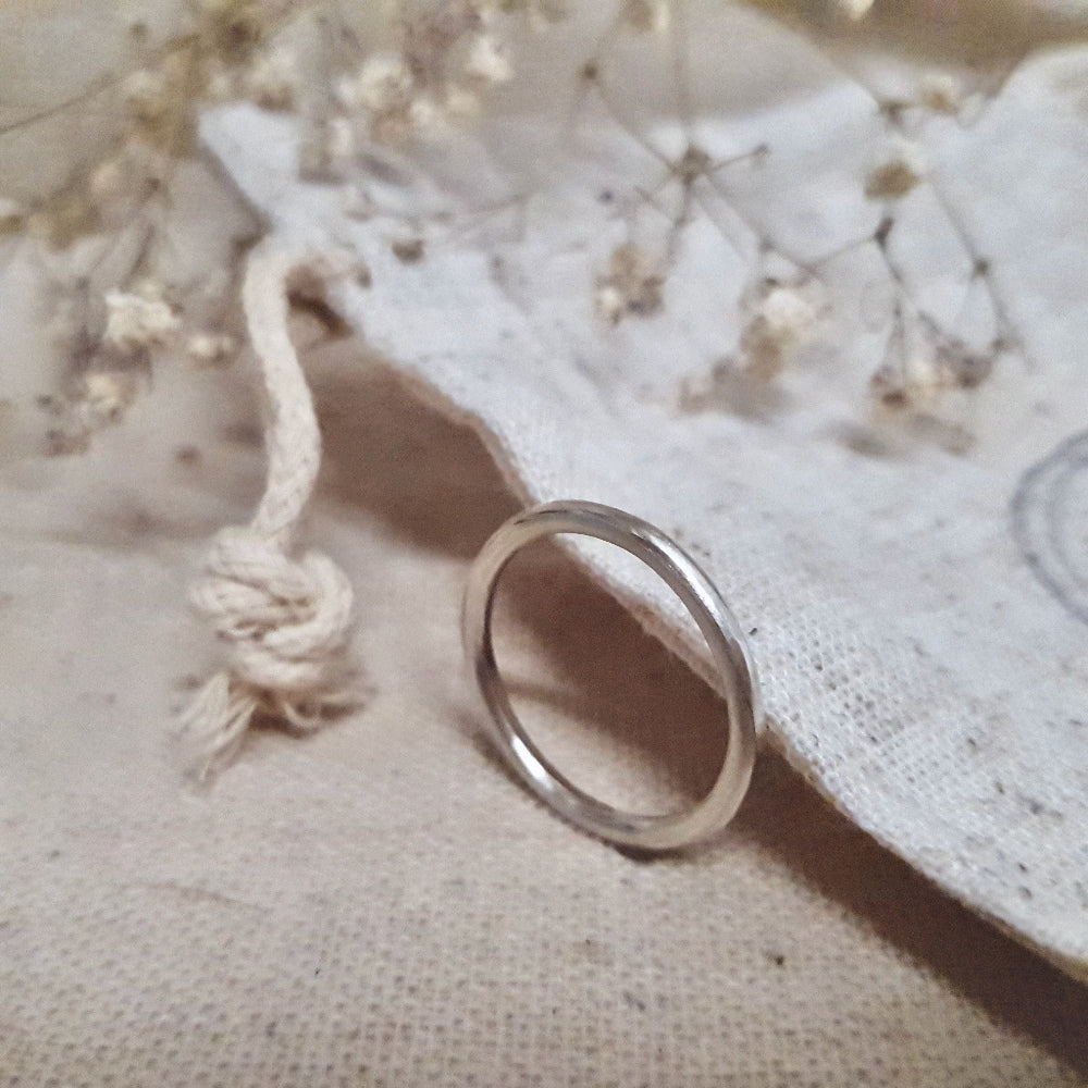 A simple silver infinity ring stood up on a beige fabric with dried flowers behind it