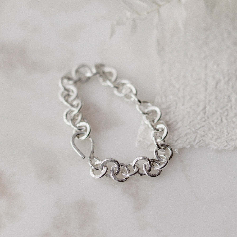 A chunky hammered link silver bracelet laid out on a white paper backround