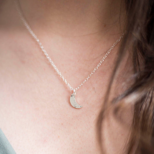 hammered silver Crescent moon pendasnt of a dainty chain being worn 